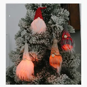 Détail de quatre gnomes de Noël lumineux avec LED suspendus sur une branche de sapin enneigée