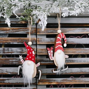 Pair of wooden Nordic Christmas gnome ornaments hanging on a snowy pine tree background