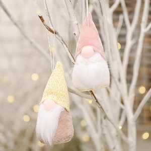 Close-up of pink and yellow plush Nordic gnomes hanging on white branches with festive lights