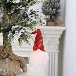 Gnome de Noël lumineux avec chapeau à étoiles rouges suspendu à une branche enneigée