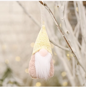 Close-up of a handmade yellow knitted Christmas gnome ornament hanging on a white branch