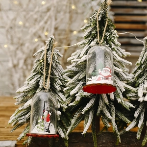 Christmas ornaments with Santa in transparent dome hanging on snowy pine branches
