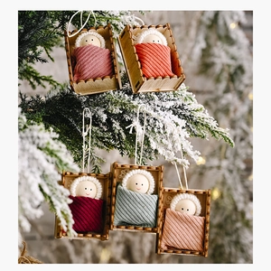 Five wooden Christmas doll ornaments hanging on a snowy pine tree with warm lights