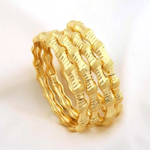 Set van vier gouden armbanden met matte en gepolijste afwerking op witte textuur stof