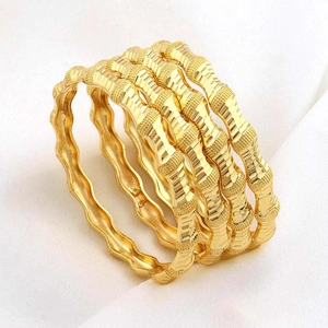 Gedetailleerd beeld van vier goudkleurige armbanden met bamboe golfdesign en matte textuur