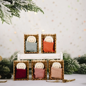 Five handmade Christmas baby doll ornaments in wooden frames with winter pine background