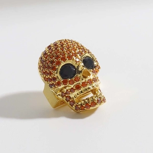 Dettaglio charm teschio dorato con zirconi arancioni e pietre preziose nere