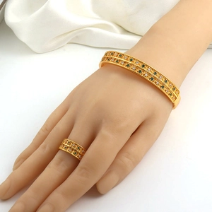 Detailed close-up of a gold-plated bracelet and ring set with green and clear zircon stones