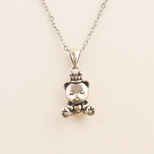 Vintage silver teddy bear necklace with crown and heart pendant on white surface