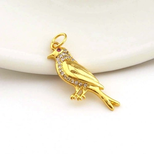 Macro detail of bird-shaped golden pendant with white zircon inlays and red gemstone eye