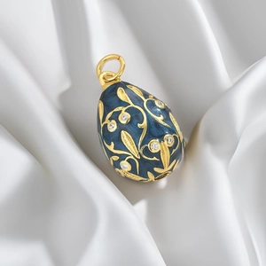 Macro detail of blue enamel Easter egg pendant with gold floral vine pattern on silk