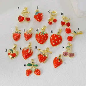 Close-up of gold-plated strawberry and cherry charms with zircon and red enamel for DIY