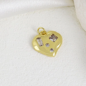 Golden heart-shaped copper pendant with various zircon stones on white silk background