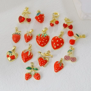 Macro detail of gold plated strawberry and cherry pendants with red zircon and enamel inlay