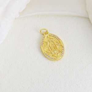 Macro shot of gold oval Virgin Mary pendant with pink zircon border on white surface