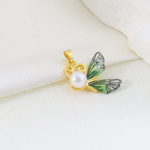 Macro detail of gold butterfly pendant with green wing, white pearl and zircon inlay