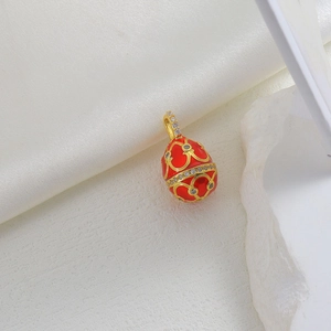 Close-up of vintage red enamel egg pendant with gold floral patterns and zircon accents