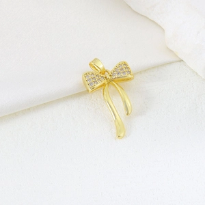 Detailed view of a gold bow pendant with zircon micro-paving and elegant metal tassels
