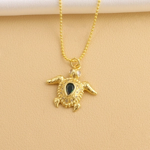 Macro detail of gold sea turtle pendant necklace featuring a teardrop green gemstone