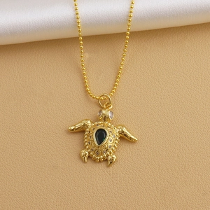 Close-up of golden sea turtle pendant with green gemstone and beaded chain detail