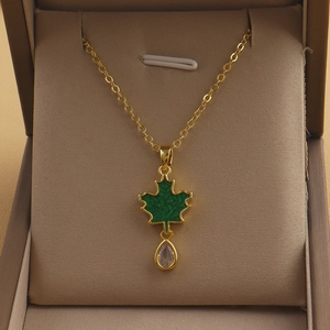 Close-up of golden necklace with green maple leaf pendant and clear teardrop crystal