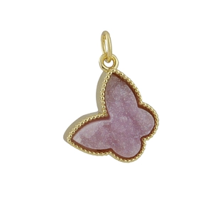 Macro shot of butterfly pendant with pink crystal texture and gold beaded metal edge
