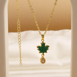 Macro view of gold chain with green enamel maple leaf and teardrop zircon pendant
