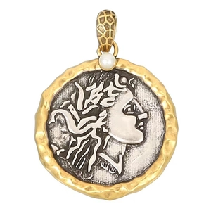 Dettaglio di un ciondolo moneta vintage con rilievo argento, trama dorata e perla bianca