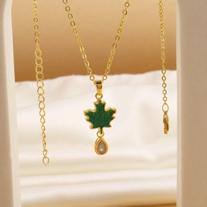 Detail of gold chain necklace with green maple leaf pendant and teardrop zircon drop