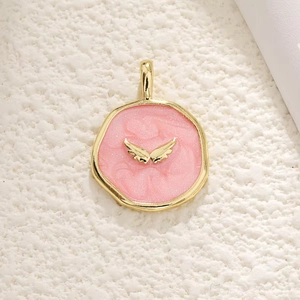 Detailed view of round pink enamel pendant with gold wings and glitter effect
