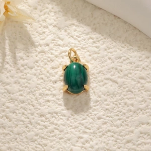 Macro shot of oval green malachite pendant in gold four-prong setting on white surface