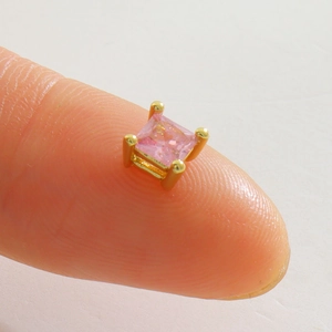 Vue macro d'un minuscule clou d'oreille carré en zircon rose sur le bout d'un doigt