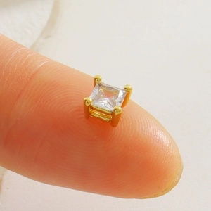 Détail macro d'une perle en zircone carrée avec monture dorée posée sur le bout du doigt