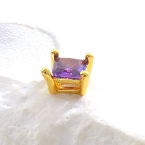 Vue macro de la boucle d'oreille en pierre carrée violette et griffes dorées