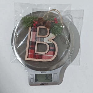 Detail showing red and black plaid Christmas letter B ornament with pine needles on a scale