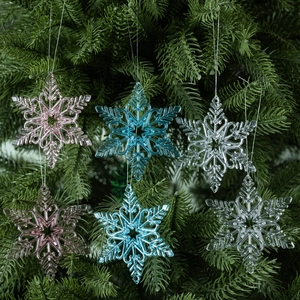 Clear acrylic snowflake ornaments in pink and blue hanging on a green Christmas tree