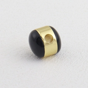 Vista macro de una cuenta negra pulida con banda central de metal chapado en oro de 18k