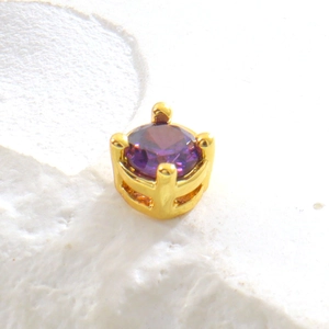 Vue macro d'une perle en cuivre doré avec cristal de zircon violet serti de micro-pavés