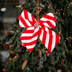 Red and white striped Christmas bow with candy center hanging on a decorated tree