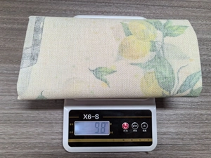 Detailed view of lemon pattern table runner fabric showing a weight of 98g on a digital scale