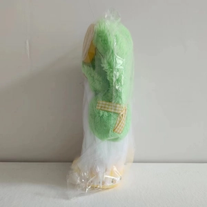 Side view of summer lemon plush gnome with green fur and yellow checkered bow in packaging