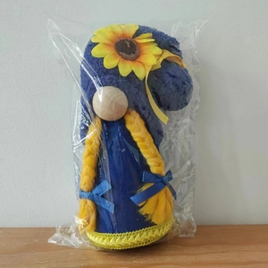 Close-up of blue and yellow gnome plush with sunflower detail in transparent packaging