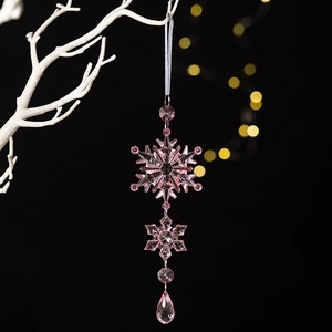 Close-up of pink acrylic snowflake and teardrop pendant hanging on white branch