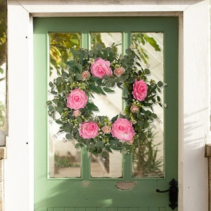 Detail of pink camellia and eucalyptus wreath hanging on a vintage green wooden door