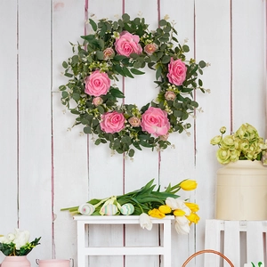 Close-up of pink camellia and eucalyptus wreath on a rustic white wood background