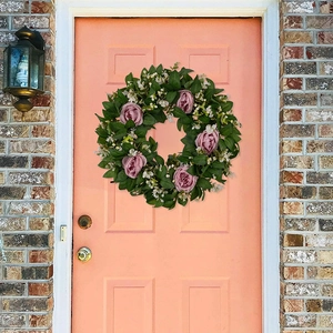 Detail eines rosa Rosenkranzes mit grünen Blättern an einer hölzernen Haustür