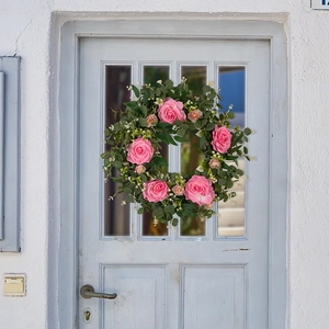 Close-up of artificial pink camellia wreath with eucalyptus leaves on a wooden door
