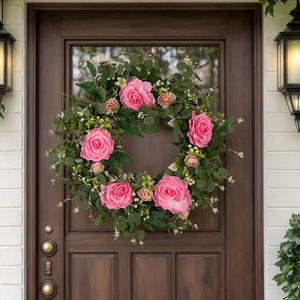 Close-up of pink camellia and eucalyptus wreath hanging on a dark wooden front door