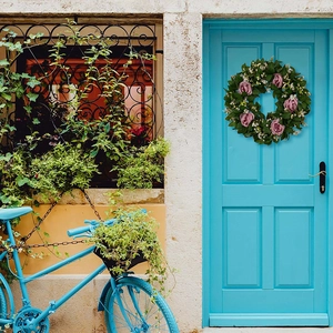 Rosafarbener Rosenkranz an einer blauen Holztür mit einem Vintage-Fahrrad-Hintergrund