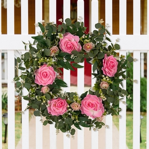 Detail of pink camellia and eucalyptus wreath hanging on a white wooden fence outdoors